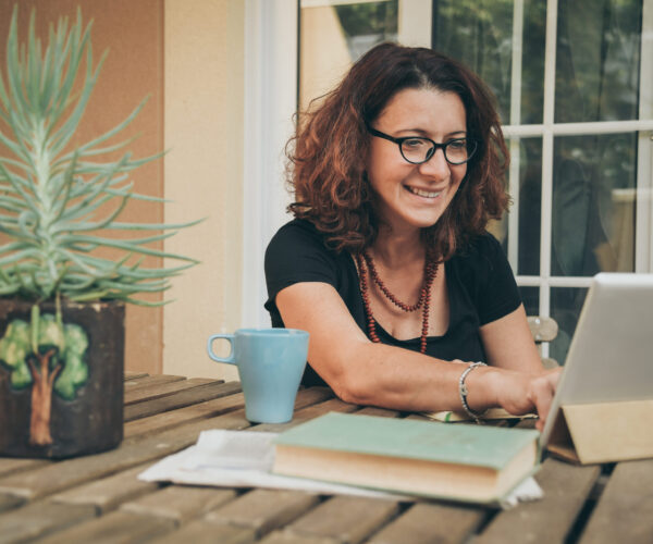 Middle aged female studying at home with books, newspaper and digital tablet pad. Woman reading a book and watching video online on new tech device. Education, modern lifestyle and leisure concept. Middle aged female studying at home with books, newspaper and digital tablet pad. Woman reading a book and watching video online on new tech device. Education, modern lifestyle and leisure concept.
