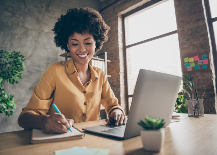 Photo of cheerful pretty cute nice girlfriend having, been employed to job as executive smiling toothily sitting at desktop with laptop noting down important information